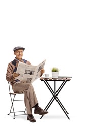 Elderly man with a newspaper sitting at a coffee table and looking at the camera isolated on white background