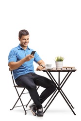 Young man sitting at a coffee table and using a mobile phone isolated on white background