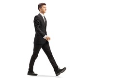 Full length shot of a young handsome man in a black suit walking isolated on white background