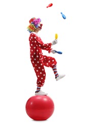 Full length shot of a clown juggling and standing on a ball isolated on white background