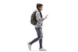 Full length profile shot of a female student with a backpack walking and looking into a mobile phone isolated on white background