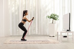 Young woman in sportswear exercising with a resistance band in front of a tv at home