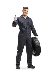 Cheerful auto mechanic worker holding a car tire and showing thumbs up isolated on white background