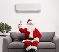 Santa claus sitting on a sofa and pointing to an air conditioning unit above mounted on the wall