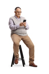 Mature man sitting on a chair and typing on a mobile phone isolated on white background