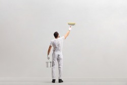 Rear view shot of a painter holding a bucket and painting a wall isolated on white background