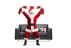 Santa claus cheering with a scarf and watching a football match in front of a black leather sofa isolated on white background