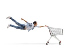 Full length shot of a casual guy man flying and holding an empty shopping cart isolated on white background