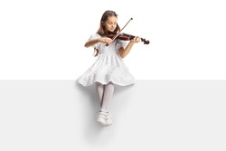 Full length portrait of a girl in a white dress sitting on a blank panel and playing a violin isolated on white background 