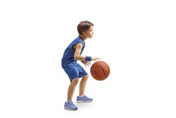 Full length profile shot of a boy in a blue jersey playing basketball isolated on white background