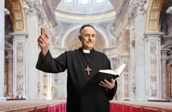 Mature male priest holding a bible and gesturing with hand inside a catholic church