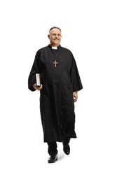 Full length portrait of a priest walking towards camera and holding a bible isolated on white background