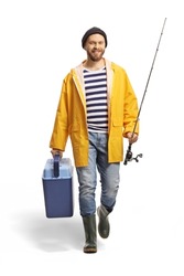 Full length portrait of a young fisherman holding a fishing rod and fridge and walking towards camera isolated on white background