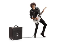 Full length portrait of a young rock musician playing a guitar plugged into an amplifier isolated on white background