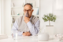 Mature man sitting on a table and using an inhalation machine at home