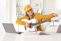 Teenage girl tunning an acoustic guitar in front of a laptop computer at home 
