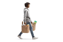 Full length shot of a young african american man carrying grocery bags and walking isolated on white background