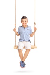 Vertical shot of a joyful little boy sitting on a swing and looking at the camera isolated on white background