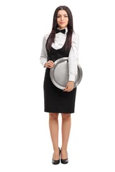 Full length portrait of a young waitress holding a round metal tray and looking at the camera isolated on white background