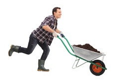 Young gardener pushing a wheelbarrow full of dirt and running isolated on white background