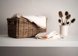 Wicker Basket with linen inside, on a shelf with a rustic bottle and dried teasel plant
