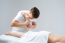 Male masseur with strong hands massaging lower part of leg to young woman lying on massage table on white background. Professional therapist men doing wellness massage shins and legs for female client