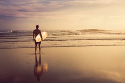 A man is standing with a surf in his hands on the sea shore. 
