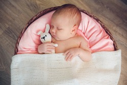 Incredible and sweet newborn baby sleeps in round basket with a toy hare (rabbit) on a wooden dark background