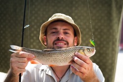 bearded man holds a caught chub fish on bait
