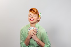 Girl with money. Closeup red head beautiful young woman pretty happy smiling pinup girl green button shirt holding euro bills earphone with one hand looking at you camera retro vintage 50's hairstyle