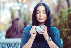 Love for coffee. Portrait of cute girl drinking enjoying her tea on the balcony over outside terrace with green bush background, wearing blue grey blouse and having breakfast, with pleasure relaxing