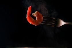 Steamed shrimp on fork isolated on dark background with copy space. Seafood buffet in restaurant concept. Use for seafood buffet promotions advertising