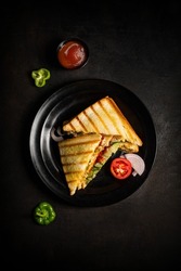 veg toast sandwich photography top angle shoot on grey-black texture background and garnish in black a plate with tomato ketchup in a bowl and some raw tomato capsicum, onion, and mint leaves.   