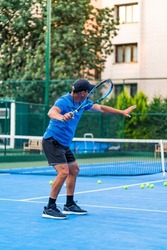 middle aged positive male tennis player coach with racket training at hard court. sunglasses