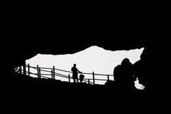 silhouette of a standing man with umbrella on a railing. The picture was taken from a cave in the direction of the exit. Black and white picture