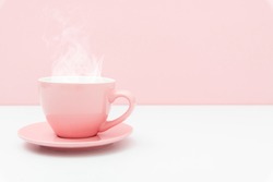 Pink cup with steam, coffee or tea on pink background.