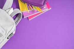 Backpack with colorful school supplies on purple background. Back to school. Flat lay, top view, copy space