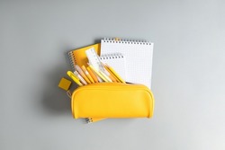 Back to school concept. Yellow school pencil case with filling school stationery, notebook, pens, pencils. Yellow school accessories on grey background. Flat lay, top view, copy space