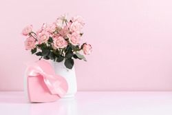 Beautiful bouquet flowers pink roses in vase and  gift box with satin bow on pastel pink background table. Birthday, Wedding, Mother's Day, Valentine's day, Women's Day. Front view