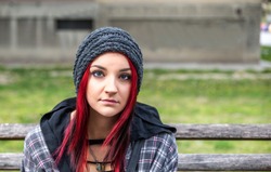 Young beautiful red hair girl sitting alone outdoors with hat and shirt feeling anxious and depressed after she became a homeless person close up portrait