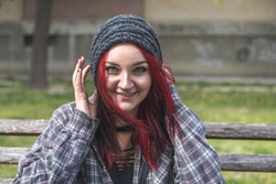 Positive smiling homeless red hair girl sitting on the bench on the street and looking in the camera  while she having fun, happy homeless concept