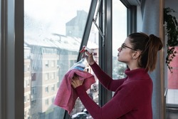 Young landlady is making a big cleaning for the apartment she is renting out, to be clean for the new tenants to whom she has rented out the apartment. Teenage girl or woman rubbing the window.