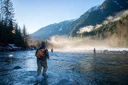A man in wader walking through the river to get to a fly fishing spot