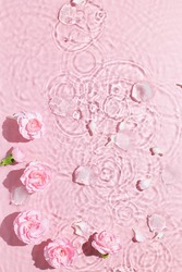 Water background. Pink aqua texture, surface of ripples, transparent, flower, shadows and sunlight. Spa and cosmetic concept background. Flat lay, top view, copy space, banner