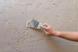 Male hands with spatula using putty for wall, builder making overhaul.