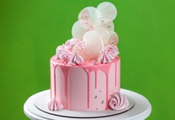 Pink cream cheese cake with chocolate chip gouges decorated with meringues and isomalt lollipops. Beautiful delicious birthday cake on the green background. Picture for a menu