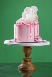 Pink cream cheese cake with chocolate chip gouges decorated with meringues and isomalt lollipops. Beautiful delicious birthday cake on the green background. Picture for a menu