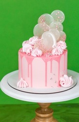 Pink cream cheese cake with chocolate chip gouges decorated with meringues and isomalt lollipops. Beautiful delicious birthday cake on the green background. Picture for a menu 