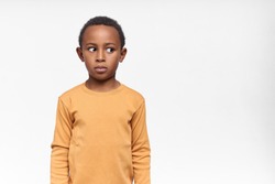 Cute funny dark skinned little boy looking away with shameful or shy facial expression, trying to hide what he has done. Black child expressing fear, being afraid of scary sudden sound, holding breath
