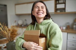 Cheerful teenage girl expressing positive emotions receiving unexpected birthday gift holding parcel and smiling with pleasure. Dark haired young woman posing with cardboard box with new cosmetics